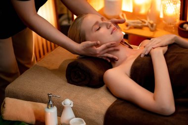 Beyaz kadın stres önleyici kafa masajı yapmaktan ve lüks otel veya otelde sıcak mum ışığında yüz güzelliği eğlencesi yapmaktan zevk alıyor. Sessiz.