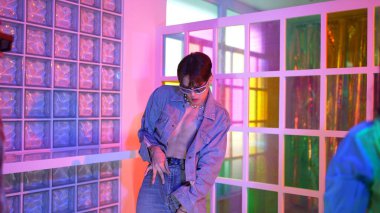 Ortasında dans eden profesyonel mutlu hipster onu alkışlayan çeşitli arkadaşlarıyla dans ediyor. Çekici Asyalı kırığı gece kulübünde neon ışığıyla enerjik adımlar atıyor. Mutluluk.