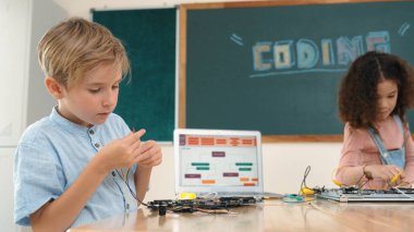 Kız tornavida kullanarak elektronik tahtayı tamir ederken ayakta duruyor. Amerikalı öğrenci ve beyaz çocuk elektrik sistemini denetlemek için birlikte çalışıyorlar. Gemide çalışan meraklı çocuklar. Pedagoji.