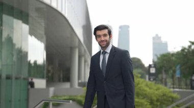 Profesyonel iş adamı hareket ediyor ve kameraya bakarken ayakta duruyor. Gülümseyen yönetici kameraya kendinden emin bir şekilde gülümsüyor. Mimari binada takım elbiseli yatırımcıların yakın çekimi. Sevinçli..