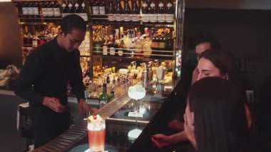 Güzel arkadaşlar lüks bir barda Paloma ve Margarita ile konuşup içerken barmen de güzel bir çiftle parti havasında kokteyl hazırlıyor. Vinosity.