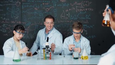 Zeki kız, çeşitli öğrenciler STEM fen dersinde deney yaparken renkli sıvıyı inceliyor. Bir grup liseli çocuk tahtada dururken laboratuvarda çalışıyor. Yaratıcı. Öğretim