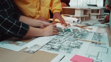 Mimari planlarla beyin fırtınası yapan ve yenilikçi inşaat ve tasarım stratejilerine odaklanan dinamik bir ekip çalışması sahnesi profesyonelleri gösteriyor. SACTR