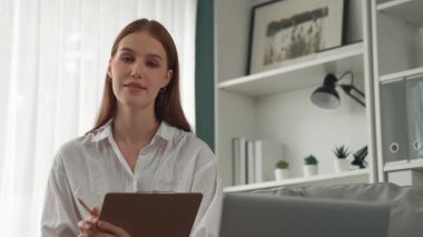 Klinikteki dost canlısı psikolog kadın. Profesyonel portresi. Kameraya bakıp psikolog muayenehanesine bakıyor. Tecrübeli ve kendinden emin psikolog.