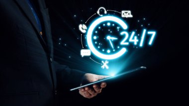 Profesyonel işadamı, dijital çağda 24 saat kullanılabilirliği ve iletişimi temsil eden ve sürekli desteği sembolize eden parıldayan bir saat simgesine sahip bir tablet tutuyor. Dörtgen