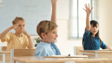 Sınıfta okuyan çeşitli çocuklarla çevrili beyaz bir çocuk öğretmenine soru sorup cevap verdiği için elini kaldırıyor. Mutlu öğrenci birlikte çalışıyor, oy veriyor, gönüllü oluyor, hocayı arıyor. Pedagoji.