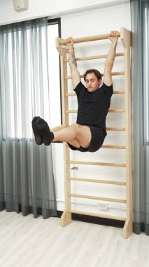 Asılı bacak egzersizi yapan mutlu bir adam vücut kaslarını güçlendirmek ve beden eğitimini iyileştirmek için duvar parmaklıkları üzerinde egzersiz yapıyor. Alt karın bölgesini iyileştirmek için erkek antrenör bacak yükseltme ameliyatı. Alışkanlık.