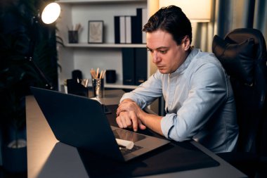 Akıllı iş adamı, gece vakti mavi perde arkasında iş hedefi olan finansal teknoloji veri raporlarını analiz etmek için veritabanı stoklarını araştırmak üzere dizüstü bilgisayarda uzaktan çalışıyor. Bireysel.