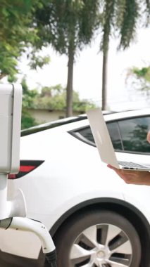 Evde EV şarj istasyonu kurulumu üzerinde çalışan nitelikli teknisyen, EV için dizüstü bilgisayarla şarj sisteminde sorun çıkarma ve yapılandırma ayarları yapıyor. Titiz