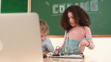 Akıllı kız tornavida kullanarak elektronik tahtayı tamir ederken ayakta duruyor. Mutlu öğrenci ve mutlu beyaz çocuk elektrik sistemini denetlemek için birlikte çalışıyor. Gemide çalışan meraklı çocuklar. Pedagoji.