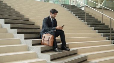 Merdivenlerde dizüstü bilgisayar ve telefon kullanarak yatırımcı çalışma ya da planlama stratejisi. Dizüstü bilgisayar kullanarak ve telefonla konuşarak veri analizi yaparken takım elbise giyen profesyonel bir iş adamı. Sevinçli..