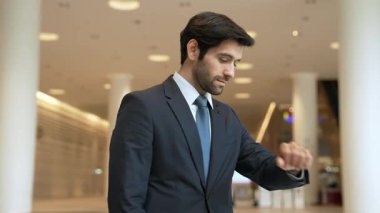 Kafkasyalı zeki iş adamı iş arkadaşını beklerken saate bakıyor. Bulanık geçmişiyle alışveriş merkezinde dikilirken yönetici takım elbise giyiyor. Yatırımcı mavi takım elbise giyer. Sevinçli..