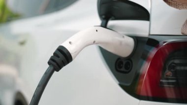 Ağır çekimde çalışan adam, alışveriş merkezinin otoparkındaki kamu EV şarj istasyonunda elektrik için akıllı telefon kullanıyor. EV aracıyla modern çevre ve sürdürülebilir kentsel yaşam tarzı
