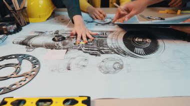 Bir grup mühendis, gerekli alet ve ekipmanlarla çevriliyken teknik planları ve taslakları tartışan bir uçak motoru tasarımı üzerinde işbirliği yapıyor. SACTR