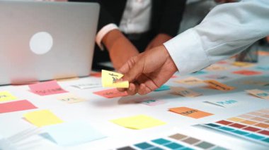 Canlı bir çalışma alanı, takım çalışmasını gösteren açık bir dizüstü bilgisayar eşliğinde masaya yayılmış renkli yapışkan notlarla birlikte işbirlikçi bir tartışmaya girişiyor. SACTR