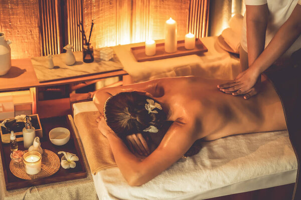 Caucasian woman customer enjoying relaxing anti-stress spa massage and pampering with beauty skin recreation leisure in warm candle lighting ambient salon spa at luxury resort or hotel. Quiescent