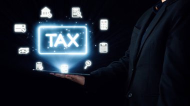 Bir işadamı, vergi idaresi ve uyum çözümlerinde finans ve teknolojinin kesişmesini sembolize eden, parlayan vergi simgelerini gösteren bir tablet tutuyor. Dörtgen