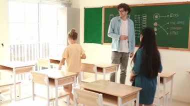 Çeşitli ilkokul öğrencileri öğretmenleri çocuğa bakarken sınıfta yürüyorlar. Profesyonel eğitmen tahtaya çıkıp öğretmenlik yapmaya hazırlanırken sevimli çocuklar sınıfa katılıyor. Pedagoji.