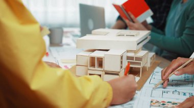 Bir grup profesyonel, modern bir çalışma alanında takım çalışması ve yaratıcılığı gösteren ölçekli bir model ve tasarım planları kullanarak bir mimari proje üzerinde işbirliği yapmaktadır. SACTR