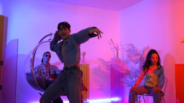 Çok kültürlü bir arkadaş kürsüde otururken Asyalı yetenekli bir dansçı modern müziğe geçiyor. Profesyonel dansçı, hipster takımı tezahürat yaparken ve desteklerken enerjik adımlar atıyor. Mutluluk.