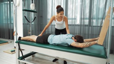 Eğitmen rehberliğinde Pilates Cadillac üzerine bar tabanlı alıştırma yapan bir müşteri. Erkek öğrenci, üst vücut gücünü arttırmak için Cadillac 'ın üzerinde kuğu esnetiyor. Alışkanlık.