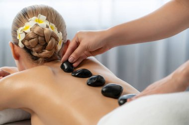 Lüks tatil köyündeki kaplıcalarda sıcak taş masajı. Gün ışığı sükunet ortamında, mutlu kadın müşteri bazalt taş masajından zevk alıyor. Rahatlatıcı bir sıcaklıkla vücudun üzerinde süzülüyor. Sessiz.