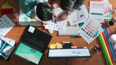 Akıllı tasarımcının renkli paletlerden renk seçmesine yardım ederken yukarıdan aşağı görünümü. Dizüstü bilgisayardan logoya bakarken birlikte çalışan ve planlayan iş adamlarının hava görüntüsü. Sempozyum.