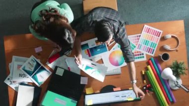 Akıllı tasarımcının renkli paletlerden renk seçmesine yardım ederken yukarıdan aşağı görünümü. Dizüstü bilgisayardan logoya bakarken birlikte çalışan ve planlayan iş adamlarının hava görüntüsü. Sempozyum.