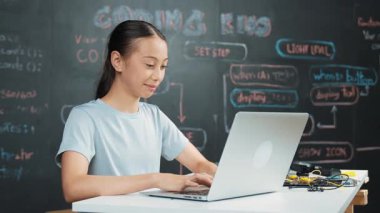Ağ geliştirme planıyla karatahtanın yanında otururken bilgisayar kodlama ve programlama sistemi kullanan beyaz bir kız. Şirin akademik öğrenci kod yazıyor ya da masada otururken bir şeyler söylüyor. Öğretim