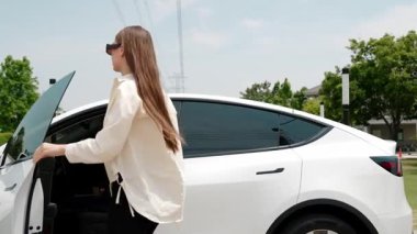 Genç kadın elektrik şebekesine bağlı elektrik şebekesine bağlı EV araba aküsünü elektrik endüstrisi olarak şarj ediyor. Çevre dostu araç kullanımı için. Yararlı