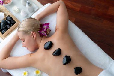 Lüks tatil beldesindeki kaplıca salonunda sıcak taş masajı. Gündüz huzurlu ortam, mutlu kadın müşteri bazalt taşı masajının keyfini çıkarıyor. Sessiz.