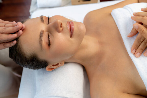 Caucasian woman enjoying relaxing anti-stress head massage and pampering facial beauty skin recreation leisure in dayspa modern light ambient at luxury resort or hotel spa salon. Quiescent