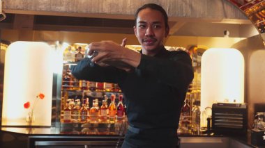 Yakın plan Asyalı barmen, lüks tezgahta karışık kokteyl sallayarak kamera önüne bakarak özel içecek menüsü hazırlıyor. Gece hayatını gösteren özel bir içecek. Vinosity.