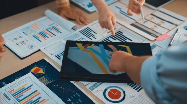 Çeşitli bir ekip, modern bir ofis ortamında veri analizi ve takım çalışması sergileyen bir strateji toplantısı sırasında tablolar ve dijital araçlar üzerinde işbirliği yapıyor. SACTR