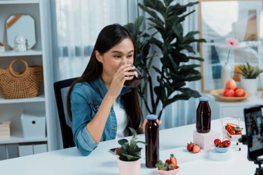 Gülümseyen, güzel Asyalı genç, lezzetli karışık çilek ve kiraz suyu detoksu içeceklerini inceleyen, sosyal medyada özel promosyon satışı için sağlıklı ürünler sergileyen. Taktik.