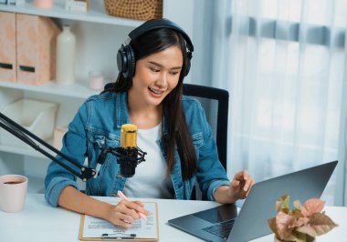 Sosyal medyada kulaklıkla canlı yayın yapan Asyalı sunucu modern stüdyoda yaşam koçluğu veya pazarlama dinleyicilerini selamlıyor. Taktik.