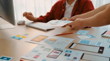 Mobil uygulama için kullanıcı arayüzü prototipini ofis çalışma alanındaki akıllı yöneticiye sunan mükemmel bir şirket çalışanı. UX UI tasarımcısı kağıt üzerinde simge tasarımının işlevini açıklıyor. Sinerjik