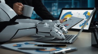 Pürüzsüz bir robotik kol dizüstü bilgisayarla etkileşime geçip veri analizi yaparken bir iş adamı modern ofis ortamında kahvenin tadını çıkarıyor.