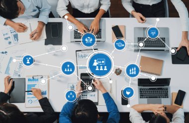 Çeşitli profesyonellerden oluşan bir grup, takım çalışması, üretkenlik ve stratejik planlamayı geliştirmek için teknoloji ve veri analizini kullanarak modern bir ofiste işbirliği yapmaktadır. Dostluk