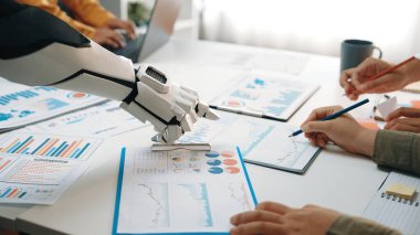 Robotik bir el, iş toplantısına katılanlara finansal raporları, verileri ve işbirlikçi takım çalışmalarını analiz etmede modern teknolojiyi sergilemede yardımcı olur.