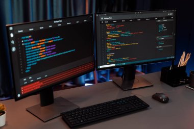 Bilgisayardaki programlama kodu masaüstü çalışma masasındaki iki ekranda akıllı web sitesi geliştirme kodlayıcı sisteminin neon ışık odasında veri teknolojisi çalıştırdığını gösteriyor. İnfobahn.