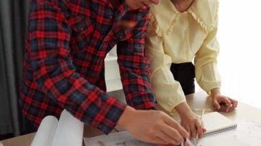 Mimarlık ve güvenlik mühendisi, modern ofiste doğruluk için mimari belge ve ölçüm aracı kullanılarak dizüstü bilgisayarın üzerinde sergilenen planlar hakkında tartıştı. - Yakın çekim. Tanımlama.