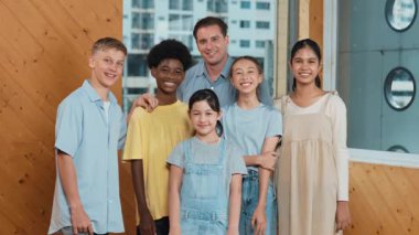 Mutlu öğretmen ve çeşitli öğrenciler kameraya gülümserken ayakta duruyorlar. Profesyonel akıllı eğitmen ve karışık ırk olan lise öğrencileri kameraya neşeli pozlar veriyor. Öğretim