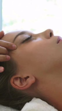 Lüks bir spa merkezinde masaj terapisti tarafından yüz masajı ve spa tedavisi için kaplıcaya uzanmış rahat bir kadın. Sağlık, stres atma ve gençleştirme kavramı.