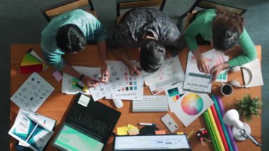 Tasarımcı fikirleri yazarken proje yöneticisinin yukarıdan aşağıya bakan görüntüsü. Akıllı iş adamları logo tasarımı fikrini açıklarken tasarımcılar palete bakarken temayı seçiyorlar. Sempozyum.