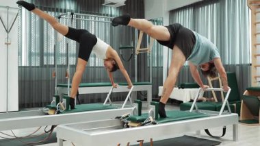 Reformist makinelerde senkronize amuda kalkma varyasyonları yapan iki pilates müşterisi. Bir grup pilates partneri kol ve çekirdeği güçlendirmek için reformcuyu ikiye ayırıyor. Denge. Alışkanlık.