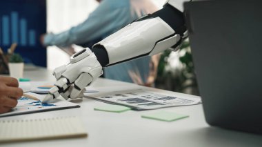 Fütürist bir robot kol, dinamik ofis ortamında bir insan işçiye yardım eder. Masa başı işbirliği ve iş dünyasındaki yenilikler üzerine mali belgeler ve grafikler. Noogenesis