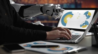 Bir insan eli dizüstü bilgisayara yazarken bir robot kol ekrana uzanıyor ve modern bir çalışma ortamında teknoloji ve yaratıcılığın karışımını gösteriyor. Noogenesis