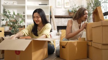 Çekici bir oda arkadaşı oturma odasında paket paketlerken pakette konum yazıyor. Mutlu satıcı birlikte çalışıyor ve teslimat paketini hazırlıyor. Girişimci kargo kutusu paketliyor. Myrmidon.