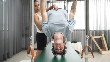 Eğitmen rehberliğinde Pilates Cadillac 'ta ters bacak yükseltme pratiği yapan sağlıklı bir müşteri. Çekirdek dayanıklılığını ve üst vücut dengesini arttırmak için Cadillac 'ı geren adam. Alışkanlık.